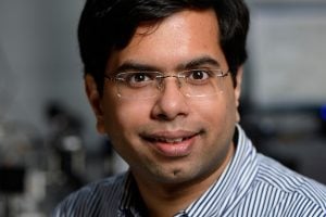 A headshot of Ishan Barman wearing a blue striped shirt in a laboratory.