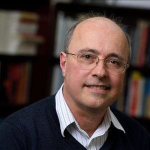 A headshot of Charles Meneveau wearing an indigo sweater over a white shirt with a blurred bookshelf in the background.