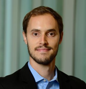 A headshot of Ryan Hurley wearing a black blazer over a blue shirt.